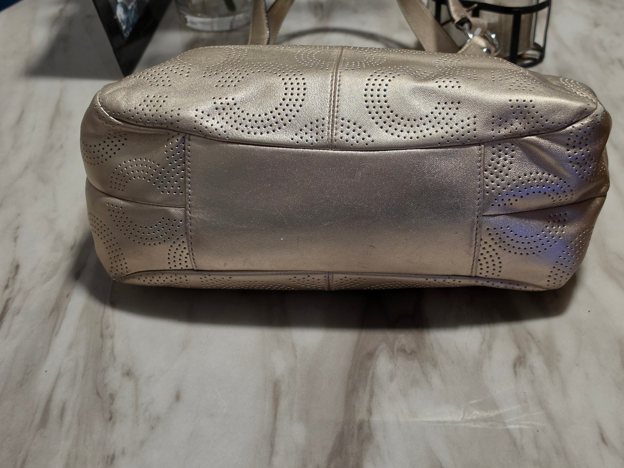 The Gettin Place Coach metallic gold leather hobo bag featuring a perforated signature pattern and silver hardware.