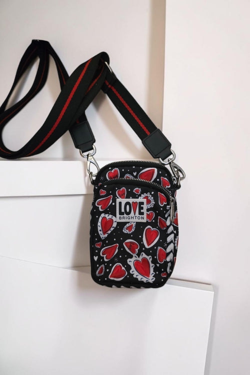 The Gettin Place black crossbody bag with red heart print, LOVE BRIGHTON patch, and adjustable red-striped strap.