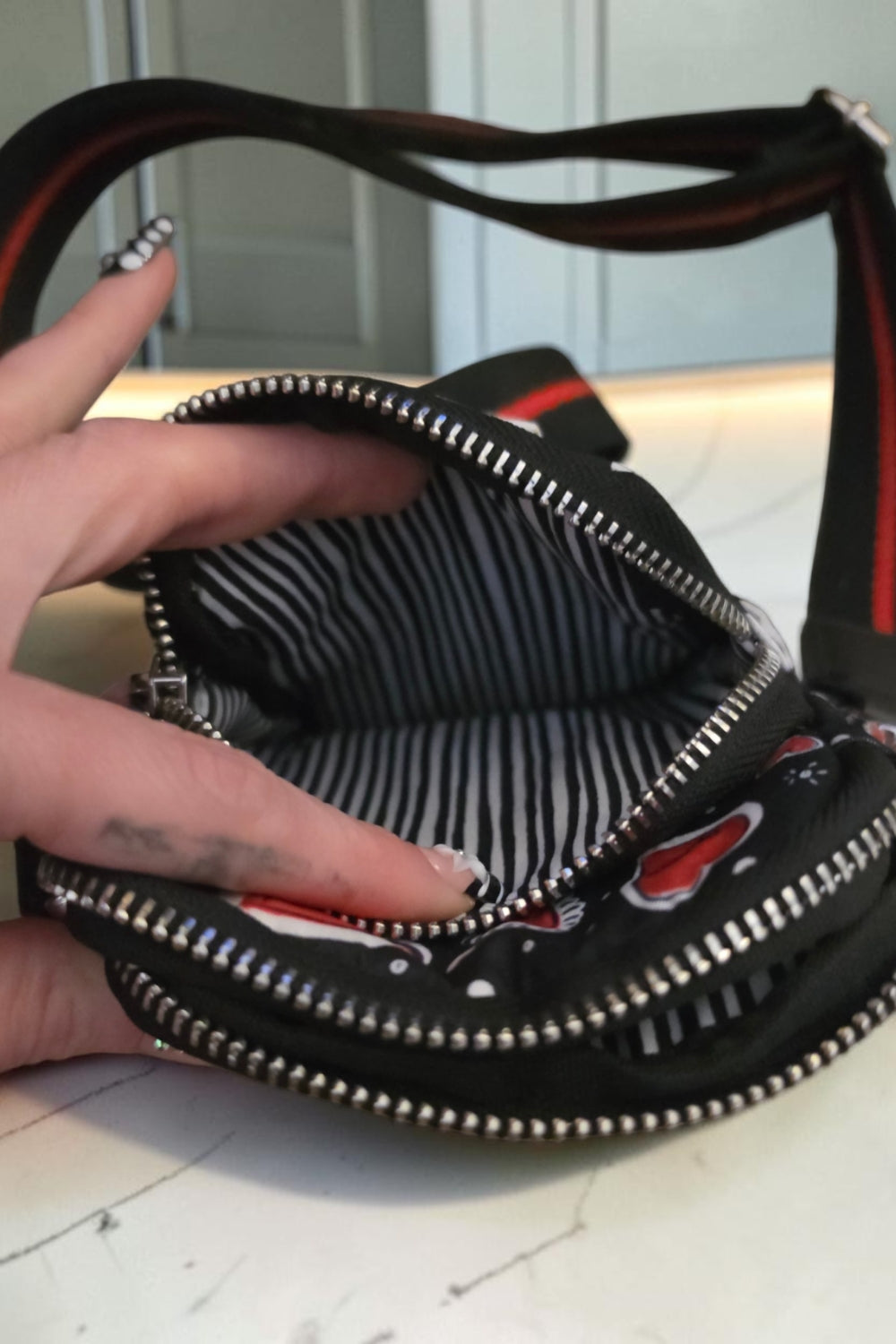 The Gettin Place black heart-print crossbody bag with silver zippers and black-and-white striped interior lining