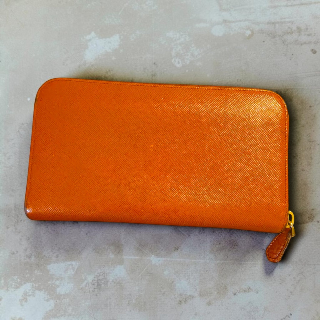 The Gettin Place orange Saffiano leather zip-around wallet with a cross-hatched texture and gold-tone zipper pull.