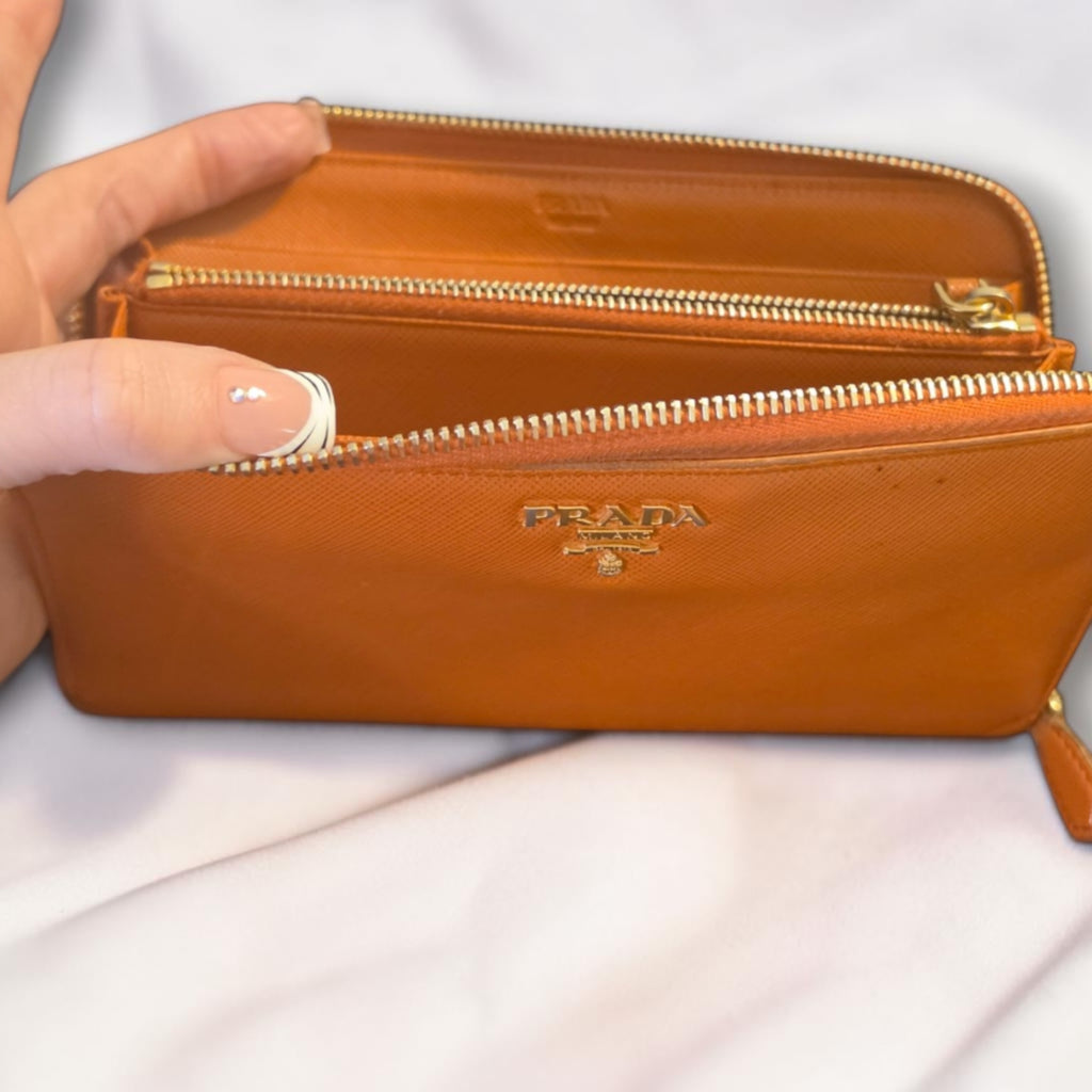 The Gettin Place orange Saffiano leather Prada zip-around long wallet with gold-tone logo plaque and interior pockets.